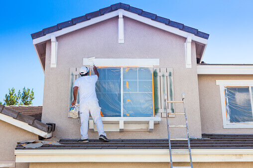 Painter rolling fresh paint onto the siding of a two-story house