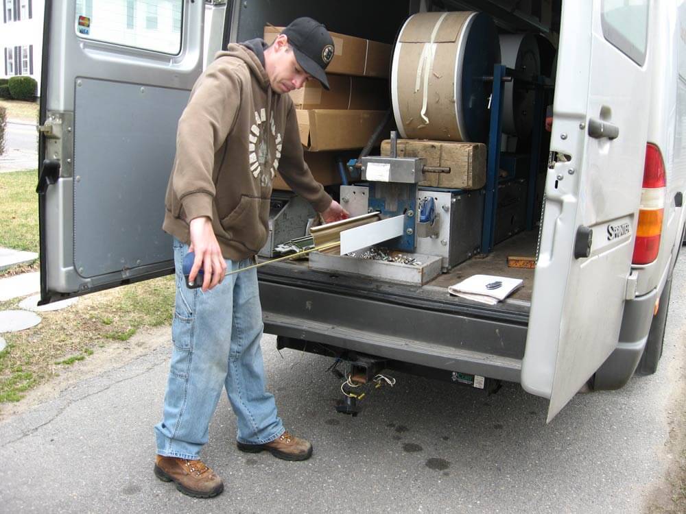 Crew member guiding aluminum coil out of a truck-mounted machine that forms one continuous gutter length